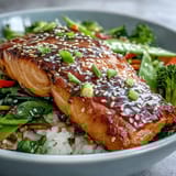 A close-up of a Teriyaki Salmon Bowl featuring tender fish, crisp veggies, and sesame garnish on steaming jasmine rice.