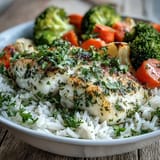 A complete Baked Tilapia Bowl with tender fish, steamed vegetables, and a fresh lemon wedge for bright flavor.