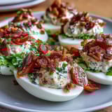 Creamy deviled eggs with smoky bacon crumbles, juicy tomatoes, and shredded lettuce, perfect for parties or brunch.  