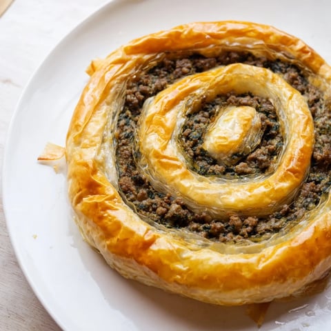 Golden, crispy Bosnian Burek pastry spiral, filled with savory beef and spinach, ready to serve.