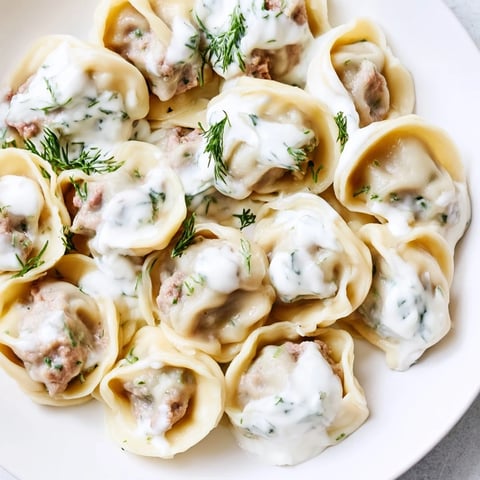 Golden Russian pelmeni, delicious meat-filled dumplings, swimming in a creamy sour cream sauce.