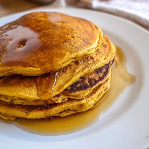 A piping-hot plate of pumpkin spice pancakes, ready to enjoy with a dollop of whipped cream.