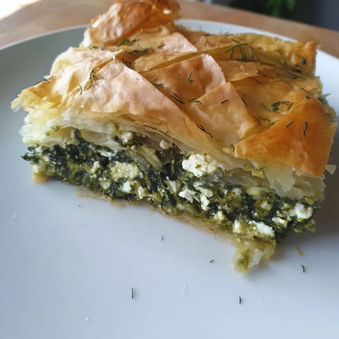 A close-up of a freshly baked Greek spanakopita, showing the crisp, golden crust and filling.