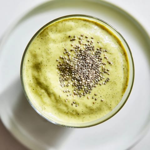 The creamy green spinach hidden smoothie, served in a tall glass next to sliced mango and a spinach leaf, highlights its refreshing tropical appeal.