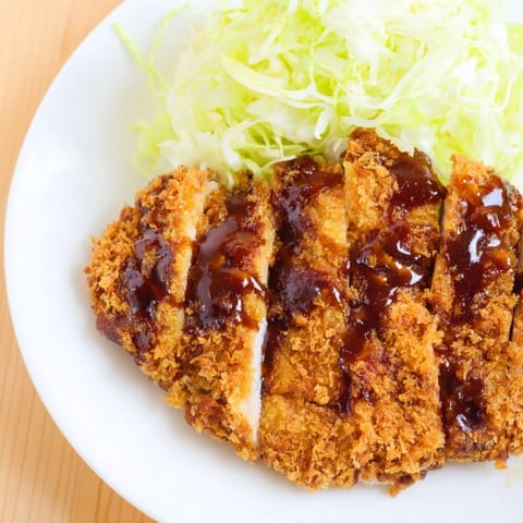 Sliced juicy chicken katsu cutlet on a bed of shredded cabbage, with lemon wedges for a fresh, bright garnish.