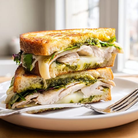 A close-up of a toasted Chicken Pesto Panini, showcasing vibrant pesto, tender chicken, and ripe tomato slices on rustic Italian bread.