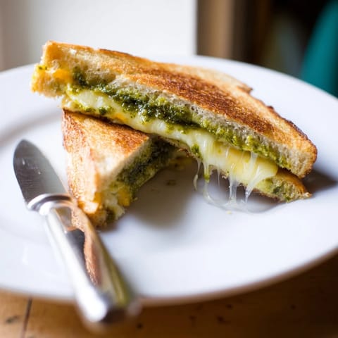 Fresh basil pesto and sharp cheddar layered between thick sourdough bread, grilled to perfection for lunch.