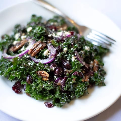 A close-up of a warm kale salad with maple mustard dressing, featuring massaged greens, toasted pecans, and dried cranberries.