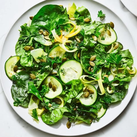 A fresh bowl of Glowing Green Salad with mixed greens and zucchini slices, sprinkled with crunchy pumpkin seeds.