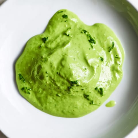 Bright green Green Goddess Dressing swirled in a white bowl, surrounded by crisp lettuce and fresh herbs.  