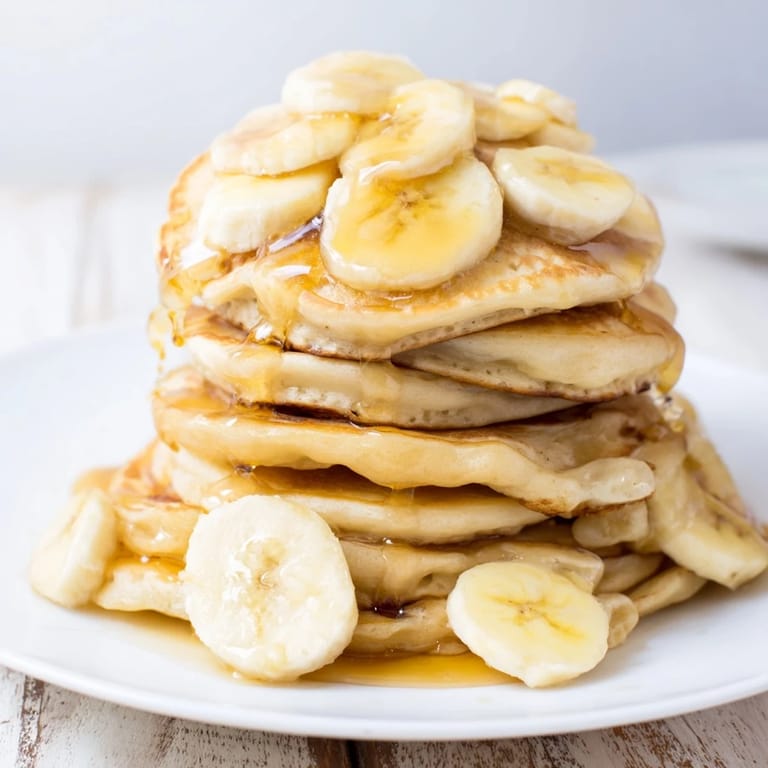 Warm maple syrup cascades over fluffy Weekend Golden-Brunch Banana Pancakes, cooked to golden perfection.