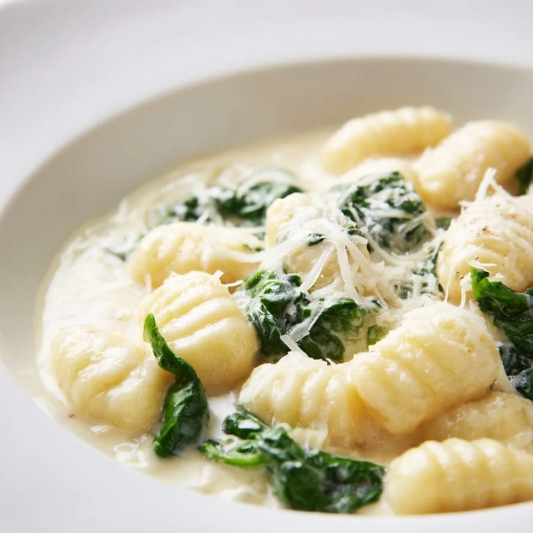 Tender potato gnocchi tossed in garlic cream sauce with vibrant spinach, ready to serve in a rustic skillet.
