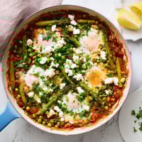 Fork-tender peas, broad beans, and asparagus simmer in a vibrant spiced tomato sauce, with runny-yolked eggs nestled in wells for a stunning vegetarian shakshuka main course.