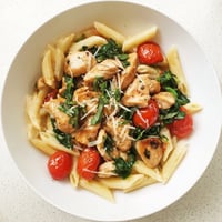 Bright yellow lemon slices and fresh green herbs garnish a steaming bowl of One-Pan Lemon Herb Pasta Chicken, served from the skillet.  